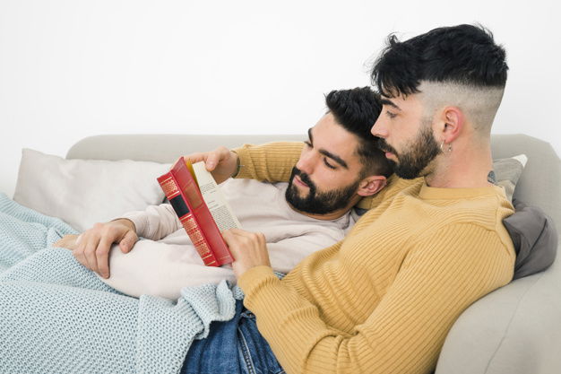 pareja-gay-acostada-sofa-leyendo-libro-casa_23-2148083010